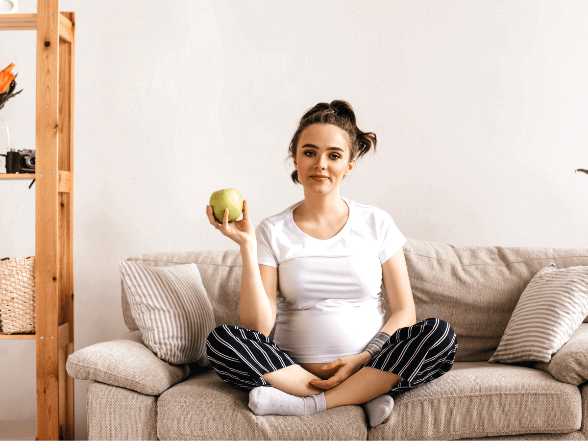 kobieta w ciąży siedzi na kanapie trzyma jabłko Bank Płodności INVICTA